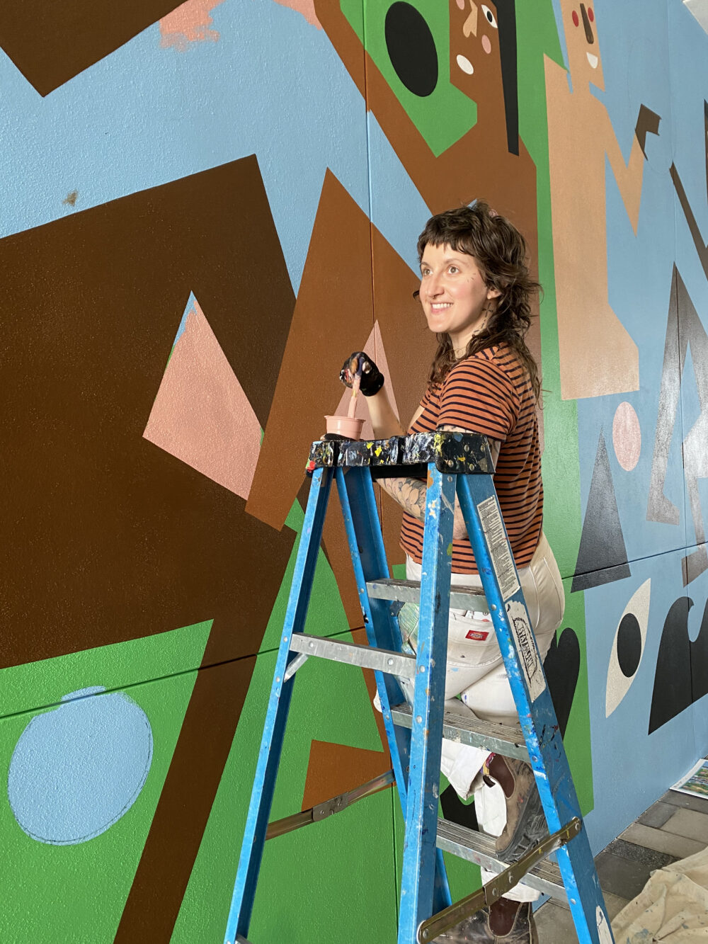 Shelby Rodeffer on a ladder in front of a mural