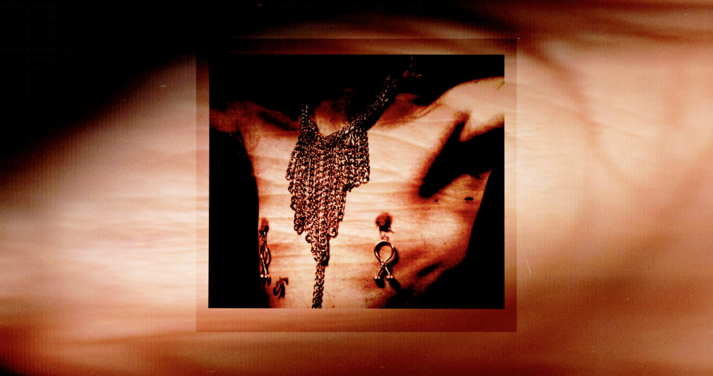 A sepia photograph on a wall of a chest with a hazy, abstracted projection atop it. The body is adorned with piercings and jewelry.
